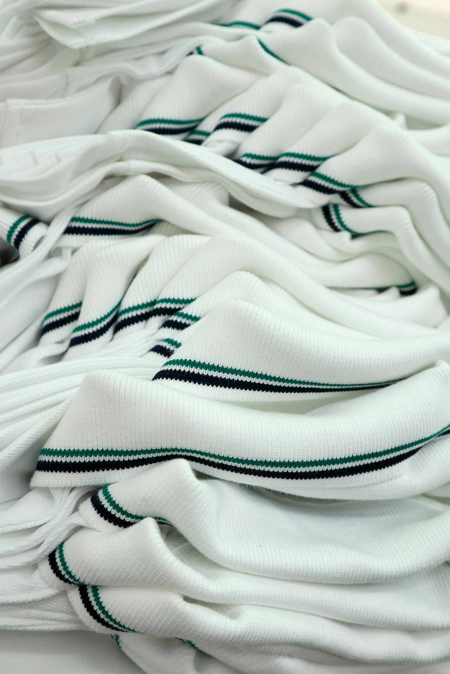 Pile of white knit fabric with black and green stripes, ideal for fashion projects.